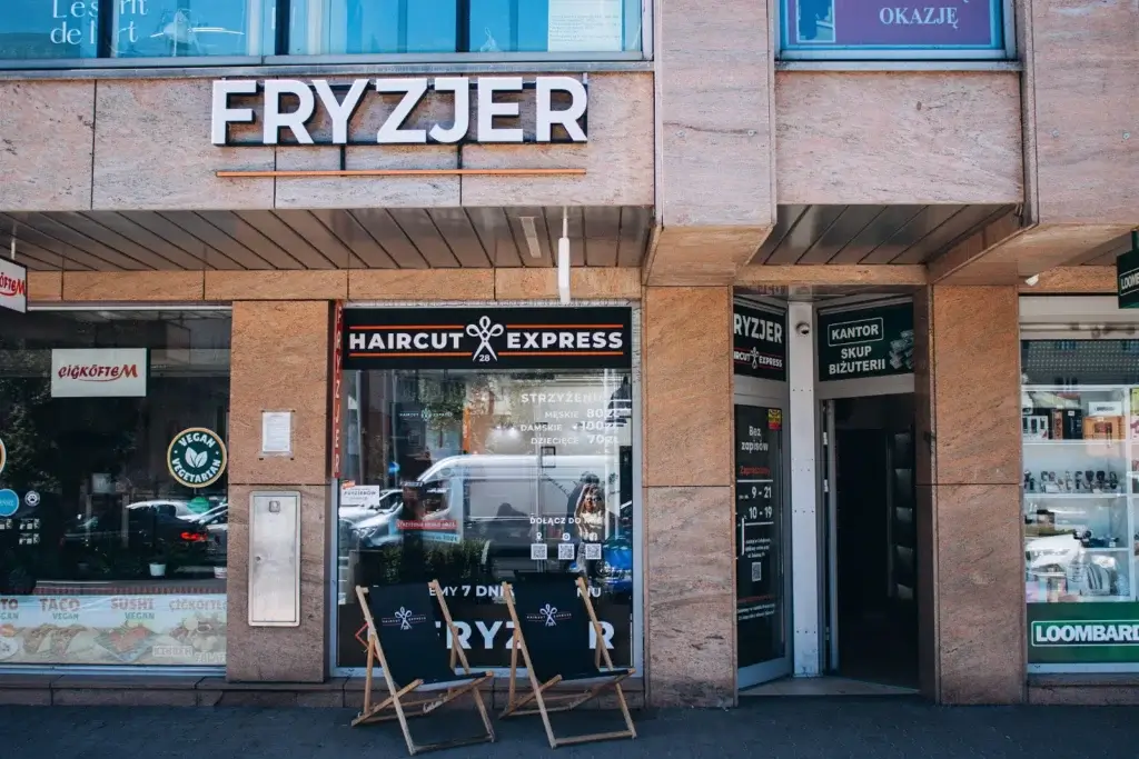 Wejście do salonu fryzjerskiego Haircut Express przy al. Jana Pawła II 41A – szyld Fryzjer, witryna z cennikiem